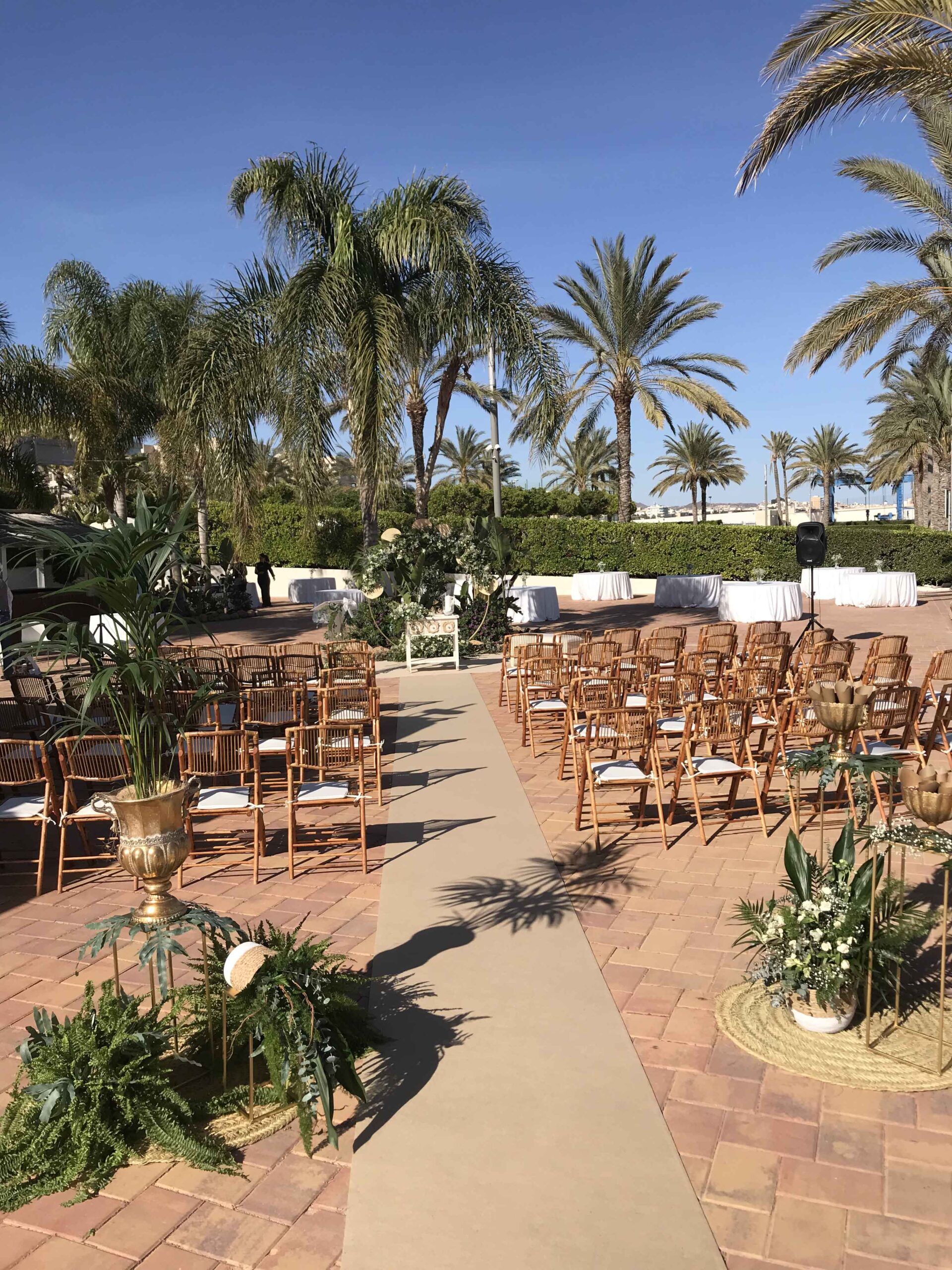 Conjunto de asientos para boda en el exterior frente al altar. Fondo decorado con palmeras.