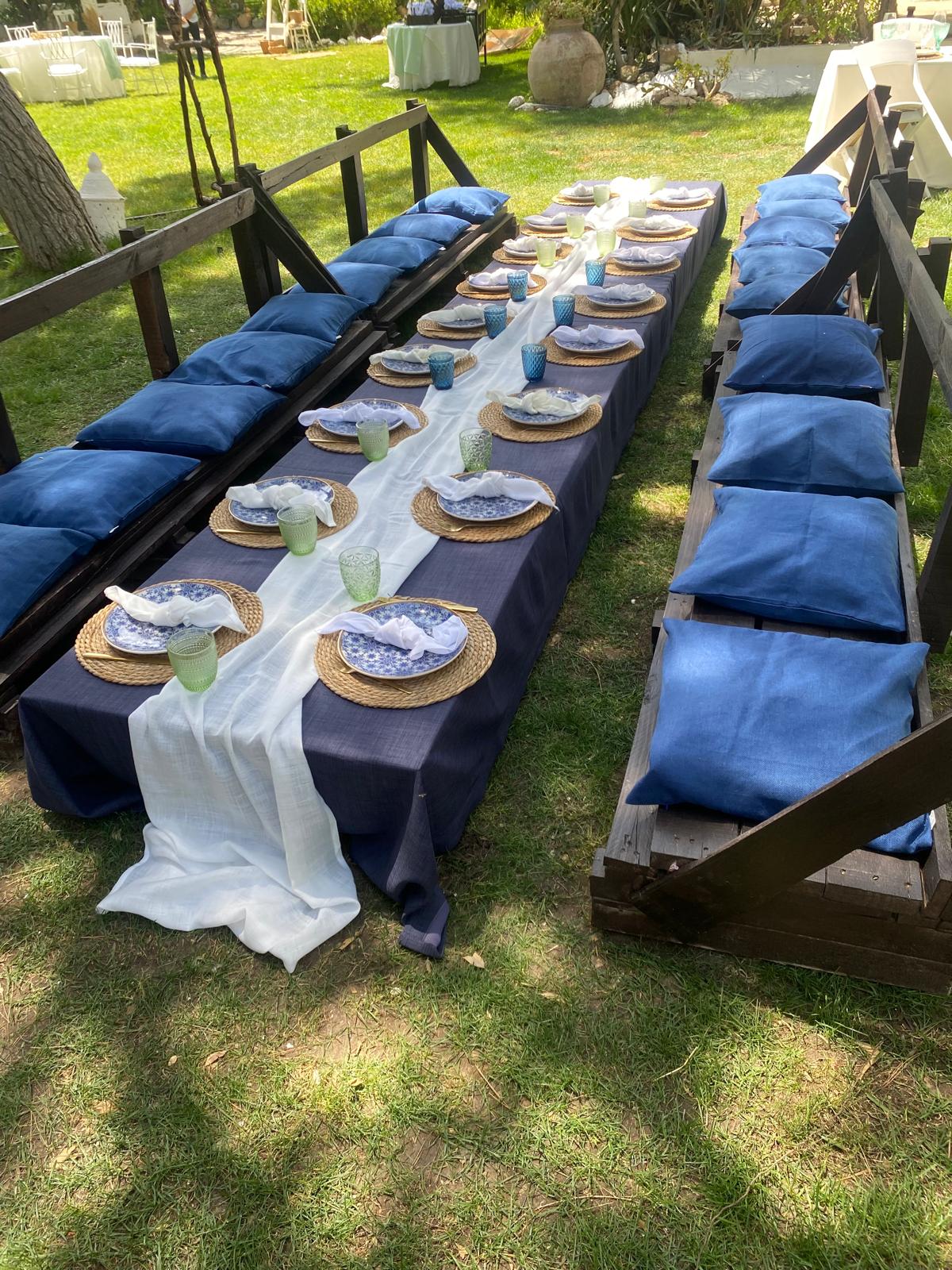 Mesa de salón exterior con asientos estilo banco rústico adornados con cojín azul marino.